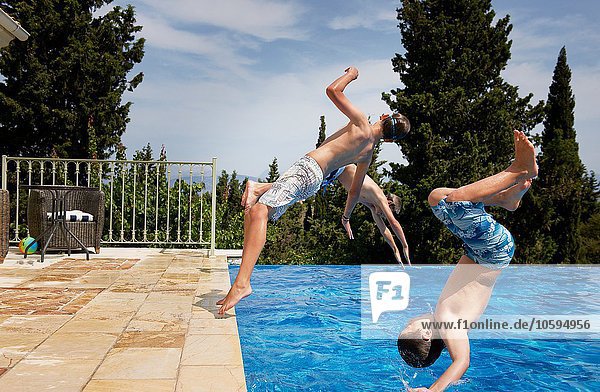 Three boys diving backward into apartment swimming pool