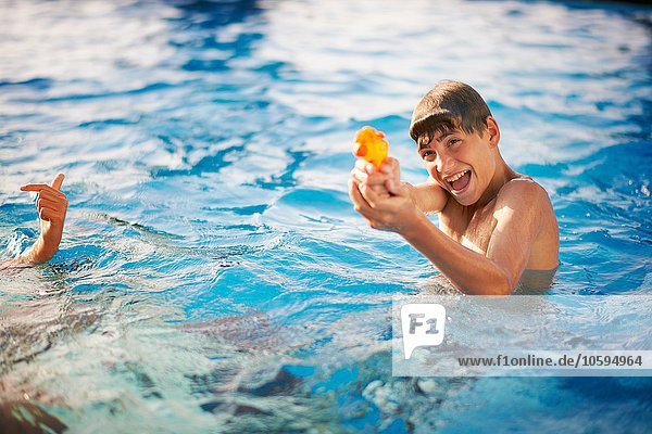 Boy squirting water pistol in outdoor swimming pool