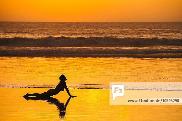 Seitenansicht des mittleren erwachsenen Frauenaktes  vorne am Strand bei Sonnenuntergang liegend  auf den Händen ruhend.