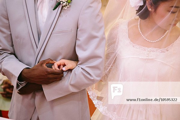 Beschnittene Ansicht der Braut mit Schleier und Bräutigam  die Händchen halten.