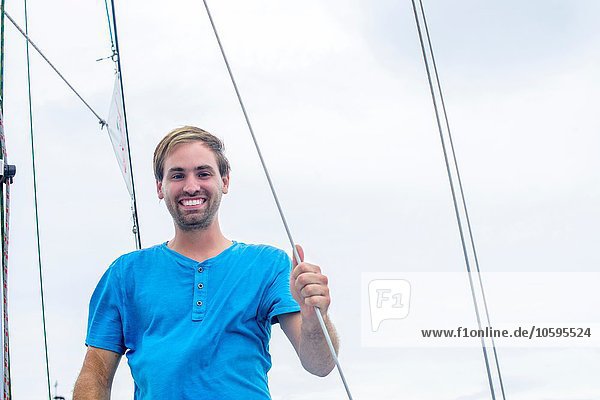 Low angle view of young man holding onto sailboat ropes looking at camera smiling