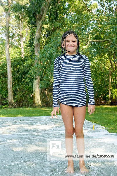 Porträt eines jungen Mädchens auf Slip n Slide Wassermatte im Garten
