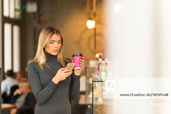 Frau mit Kaffee zum Mitnehmen per Smartphone