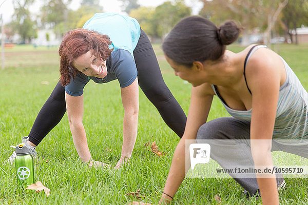 Junge Frauen  die Sportbekleidung auf Gras tragen  beugen sich von Angesicht zu Angesicht über Stretching.