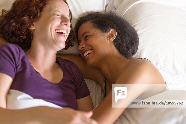 Hochwinkelansicht eines lesbischen Paares  das im Bett liegt und sich umarmt.