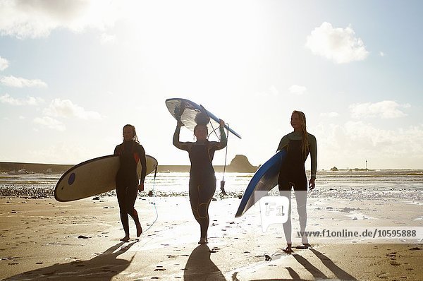 Three female friends on beach  holding surfboards