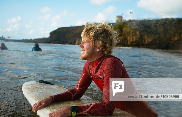 Männlicher Surfer im Meer  hält Surfbrett  ruhend
