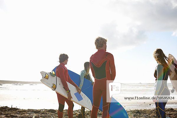 Group of surfers standing on beach  holding surfboards  rear view