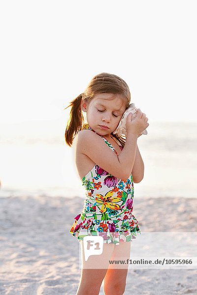 Porträt eines Mädchens  das am Strand Muscheln hört  Sanibel  Florida  USA