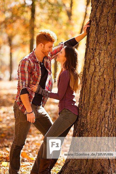 Romantic young couple leaning against tree in autumn forest