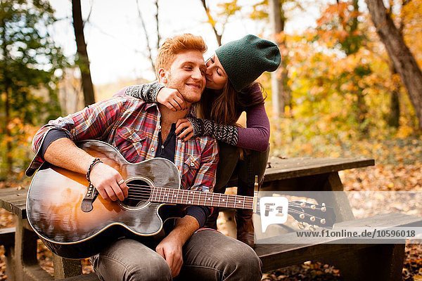 Romantic young couple playing guitar on picnic bench in autumn forest