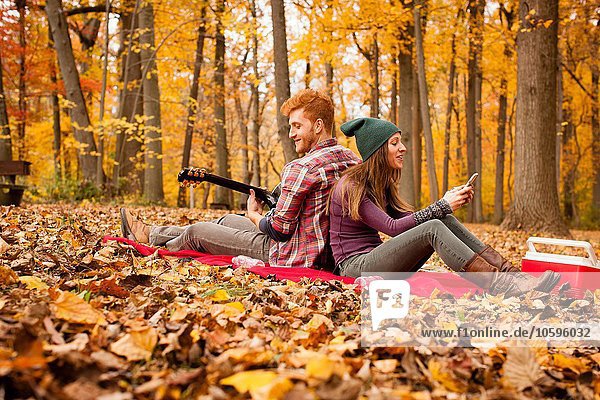 Young couple back to back on picnic blanket in autumn forest
