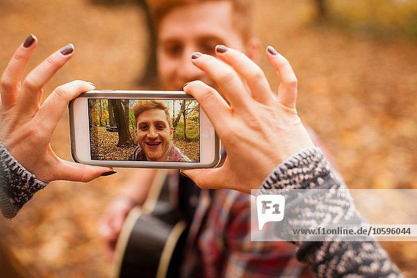 Hands of young woman photographing boyfriend on smartphone in autumn forest