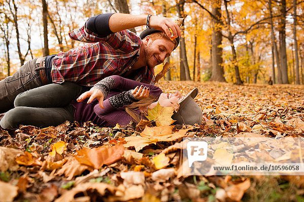 Young couple play fighting with autumn leaves in forest