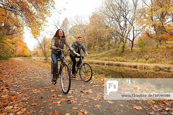 Happy young couple cycling along riverside in autumn