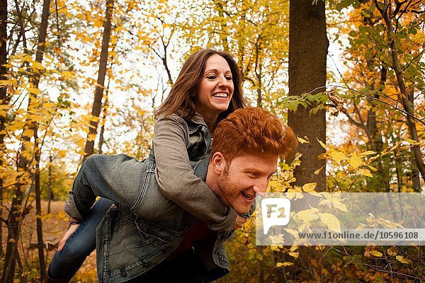 Junger Mann gibt Freundin ein Huckepack durch den Herbstwald
