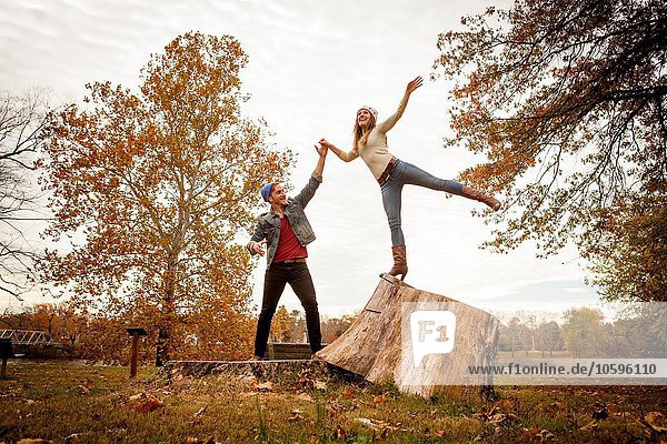 Junges Paar spielt auf Baumstumpf im Herbstpark