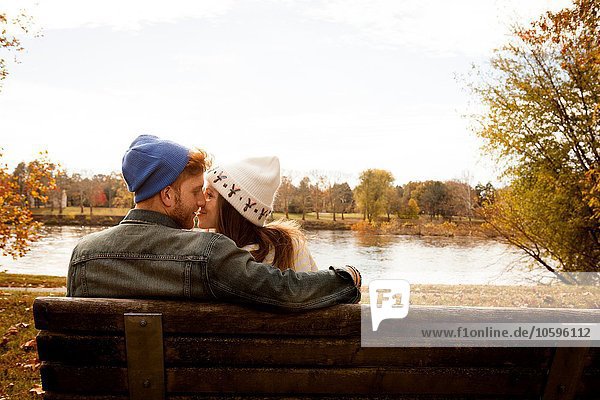 Romantisches junges Paar auf der Parkbank am Seeufer
