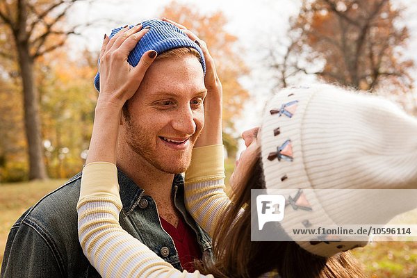 Romantic young woman adjusting boyfriends knit hat in park