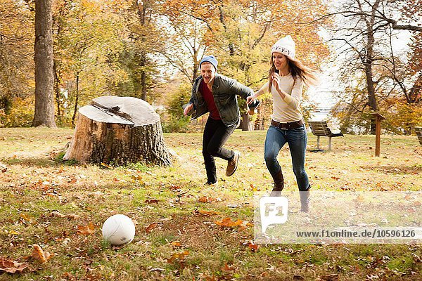 Young couple running after soccer ball in autumn park