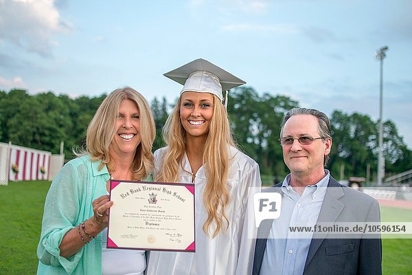 Portrait of young female graduate with parents at graduation ceremony