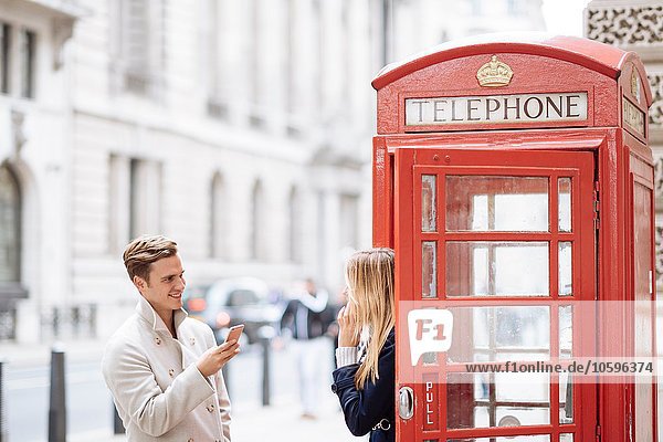 Junges Paar mit Smartphone neben roter Telefonzelle,  London,  England,  UK