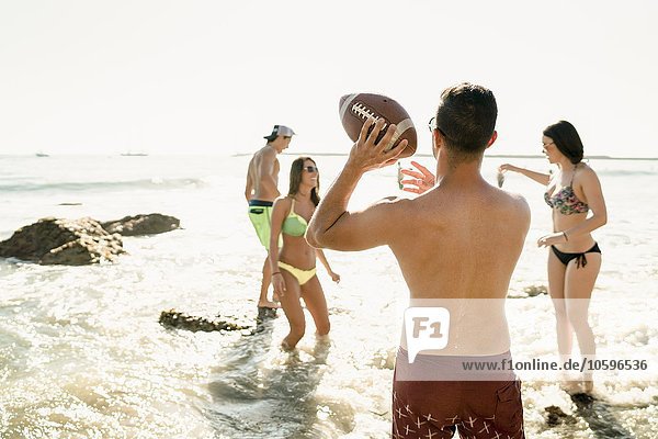 Junge erwachsene Freunde beim American Football im Meer in Newport Beach  Kalifornien  USA