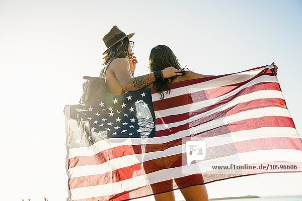 Rear view of young couple wrapped in American flag on Newport Beach  California  USA