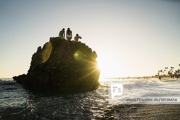 Silhouette erwachsener Freunde auf einer Felsformation bei Sonnenuntergang  Newport Beach  Kalifornien  USA