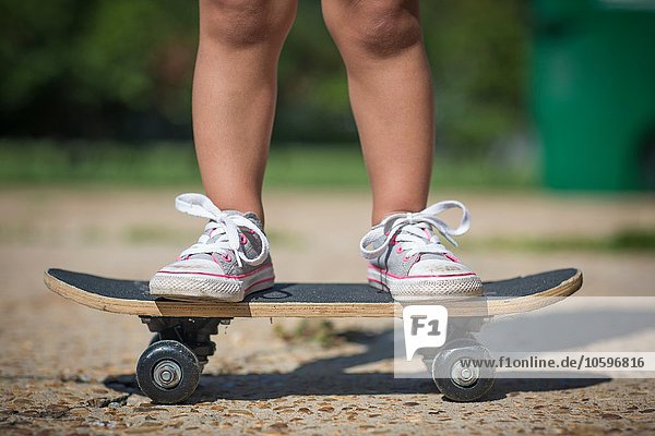 Beine des Mädchens mit Leinenschuhen auf dem Skateboard stehend