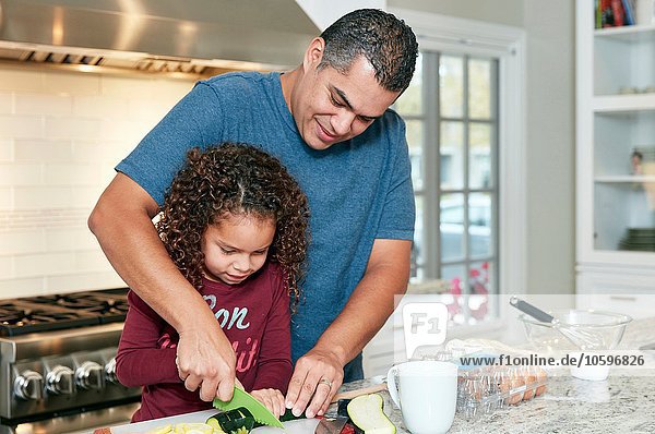 Father helping daughter chop vegetables in kitchen