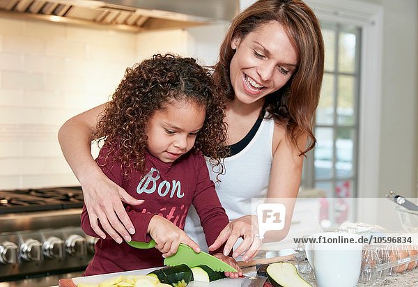Mother helping daughter chop vegetables in kitchen