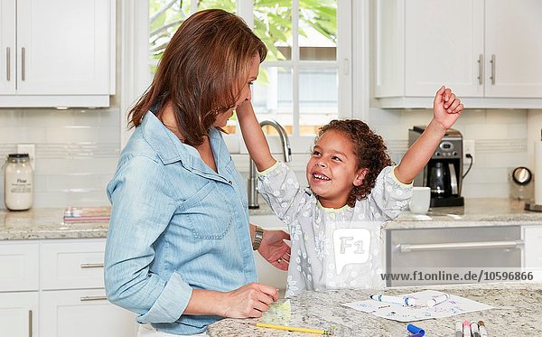 Mother and daughter at kitchen counter drawing pictures  arms raised triumphantly  smiling