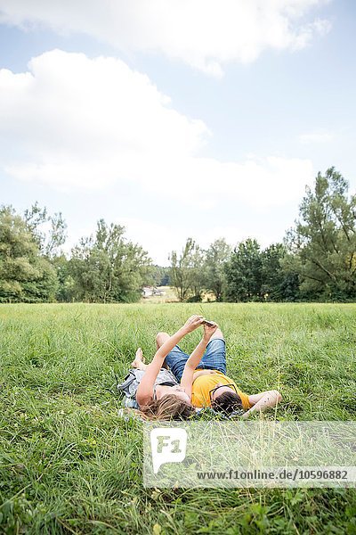 Junges Paar  das auf Gras auf dem Feld liegt und sich mit dem Smartphone selbst porträtiert.