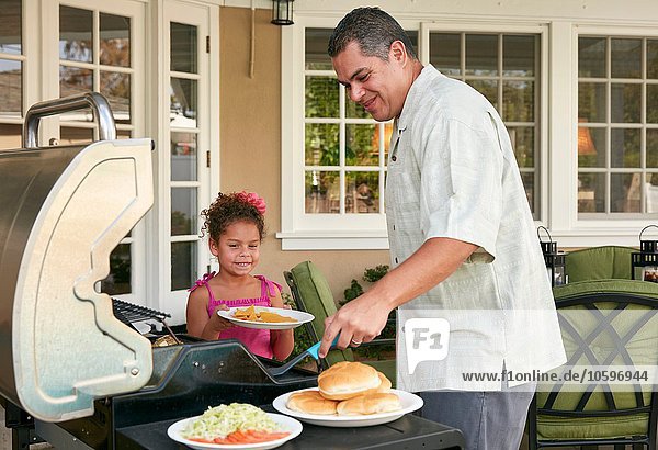 Father and daughter on patio grilling barbecue food smiling