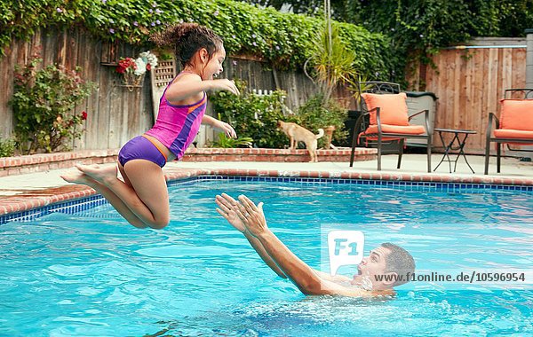 Side view of father catching girl jumping into swimming pool  in mid air