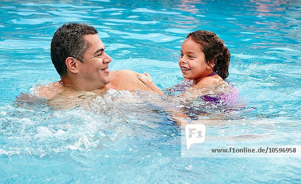 Head and shoulders of father and daughter in swimming pool smiling