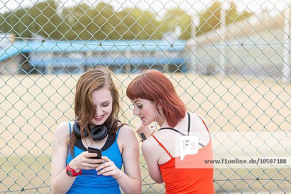Young women using smartphone beside fence  London  UK