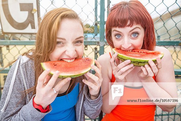 Young women eating watermelon beside sports ground  London  UK