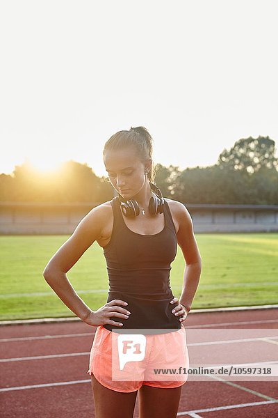 Young female runner on race track with hands on hips