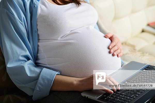Pregnant woman sitting on sofa  using laptop  mid section