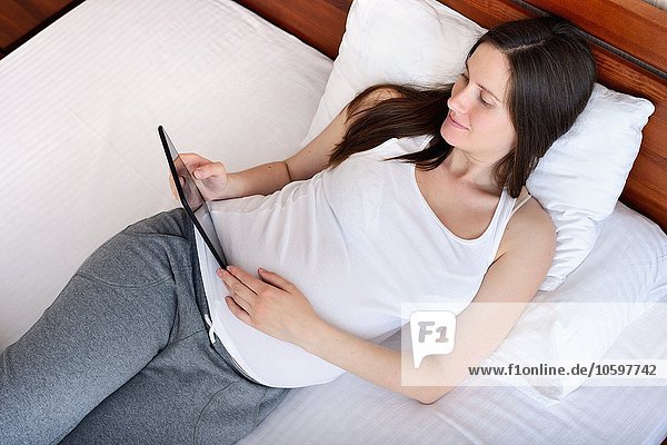 Pregnant woman lying on bed  holding digital tablet