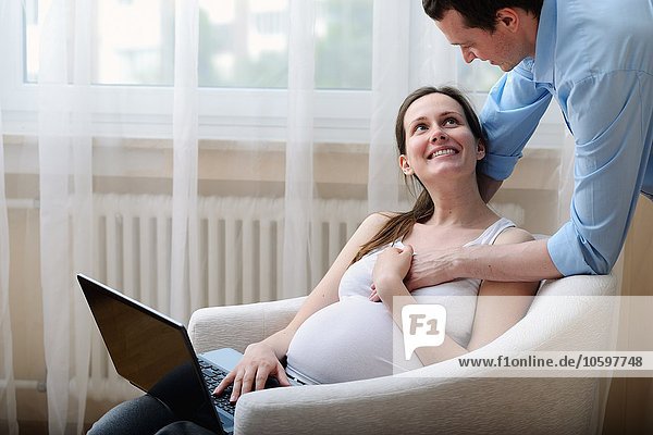 Pregnant woman sitting in chair  using laptop  husband holding her hand