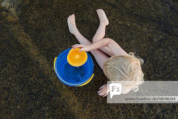 Draufsicht auf das im Sand spielende weibliche Kleinkind mit Spielzeugeimer