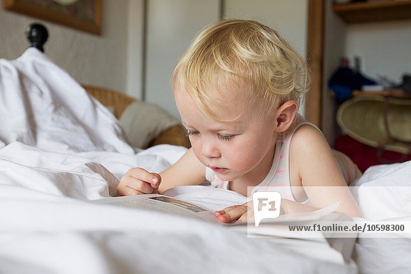 Female toddler lying in bed reading a book
