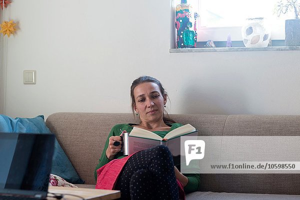 Front view of mid adult woman sitting on sofa looking down reading book