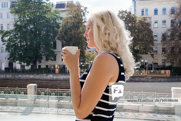 Seitenansicht einer reifen Frau im Freien  die eine Kaffeetasse in der Hand hält.