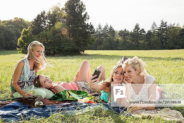 Women lying on fronts on grass using smartphone to take selfie smiling