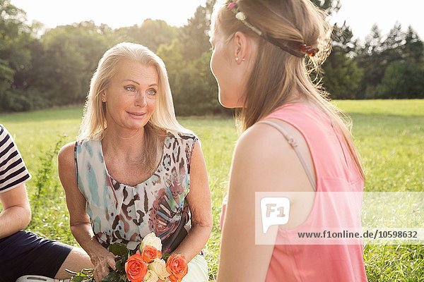 Mature woman holding flowers sitting in field talking to young woman