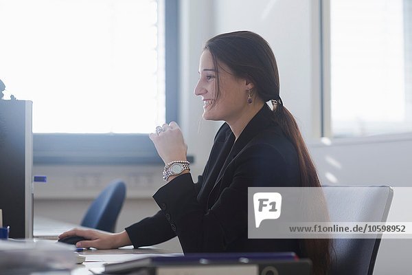Side view of young woman in office sitting at desk using computer smiling
